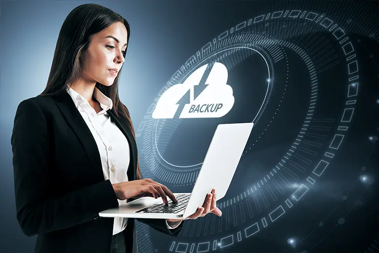 Businesswoman using a laptop with a digital cloud backup icon and data graphics in the background.