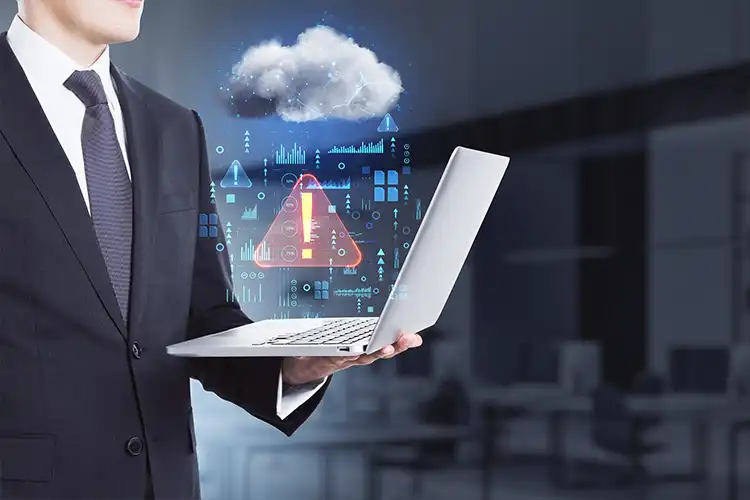 A person in a business suit holds a laptop with digital cloud and warning icons floating above, symbolizing cloud computing, data alerts, and technological analysis.