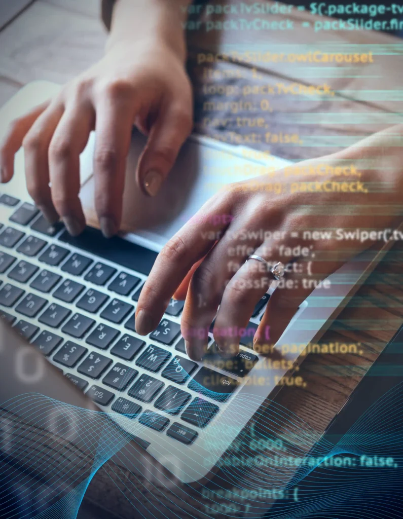 Person typing on a laptop with overlaid programming code and digital graphics, emphasizing coding and technology.