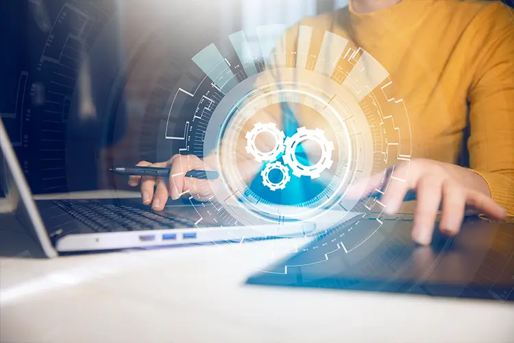 A person working on a laptop and tablet with digital gear and technology graphics overlay, representing innovation and digital transformation.