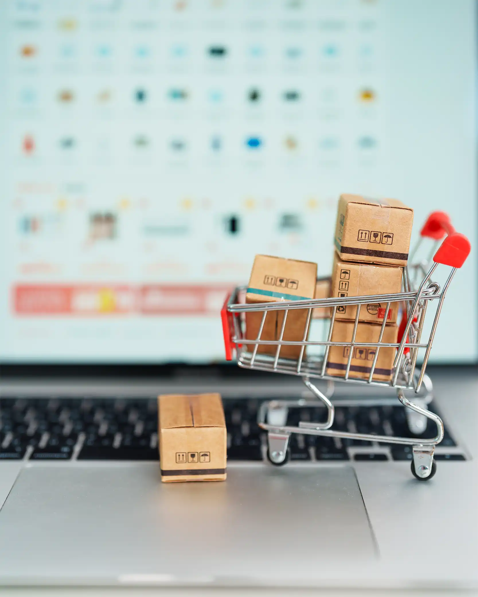 Small cardboard boxes in a shopping cart on a laptop keyboard with a blurred computer screen in the background.