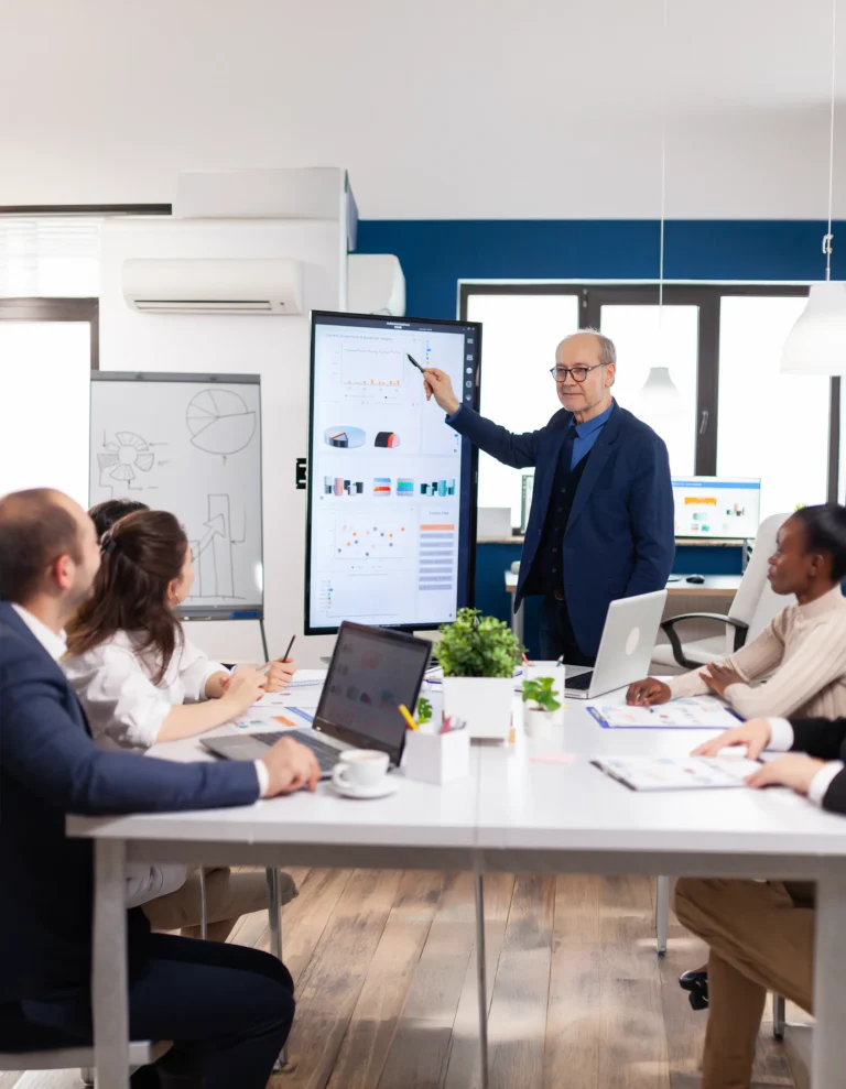 Business meeting with a presenter explaining data on a large screen to colleagues in a bright office.