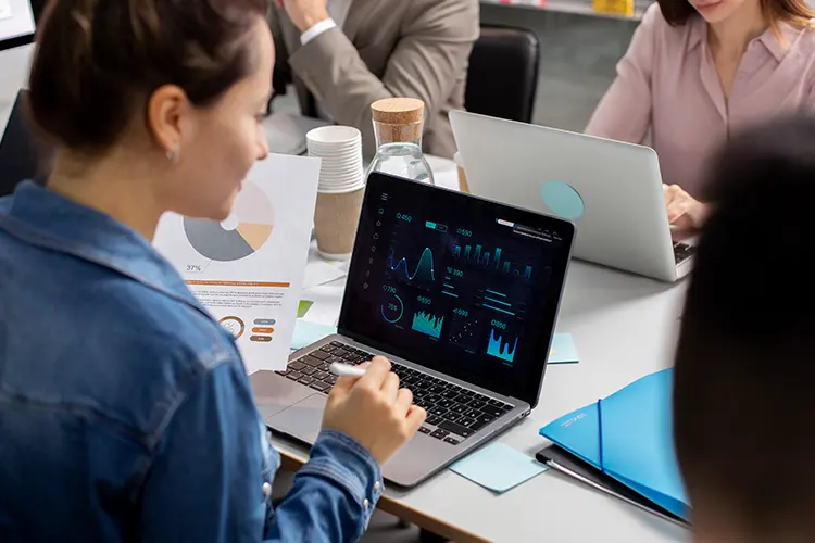 Businesswoman analyzing data on a laptop with charts and graphs during a team meeting in a modern office.