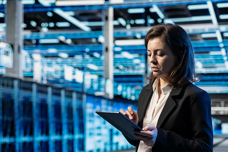 Businesswoman in a warehouse using a tablet, with shelves and blue lighting in the background.