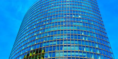 A tall, curved glass building with a grid pattern of windows against a blue sky.